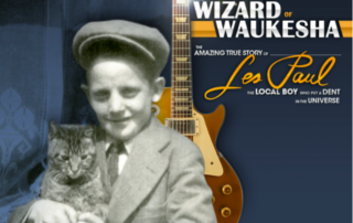 Exhibit poster titled “The Wizard of Waukesha,” featuring a vintage photograph of a child holding a cat beside a guitar, with text about the true story of Les Paul.